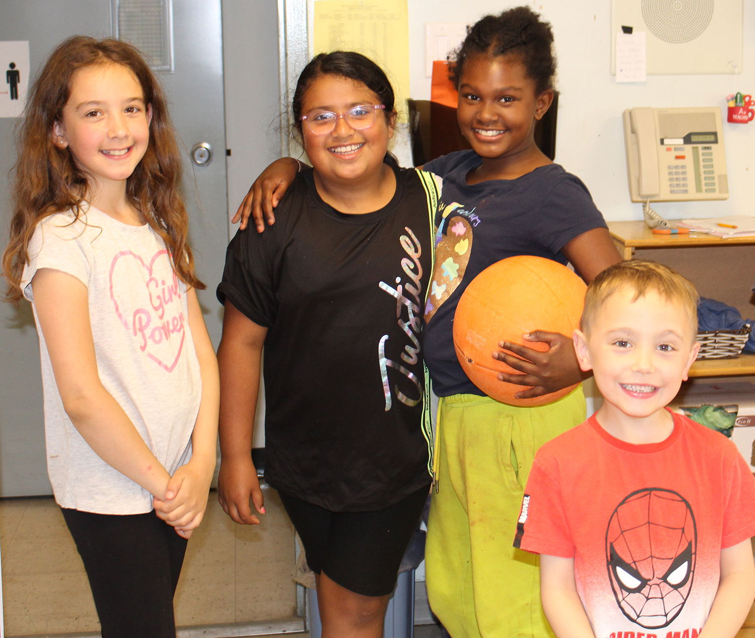 A group of children in a PLASP classroom stand in a group smiling