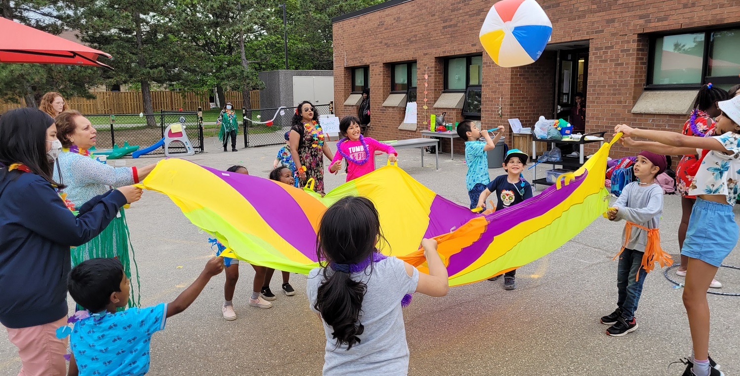 PLASP children and educators bounce a beach ball on a parachute outside