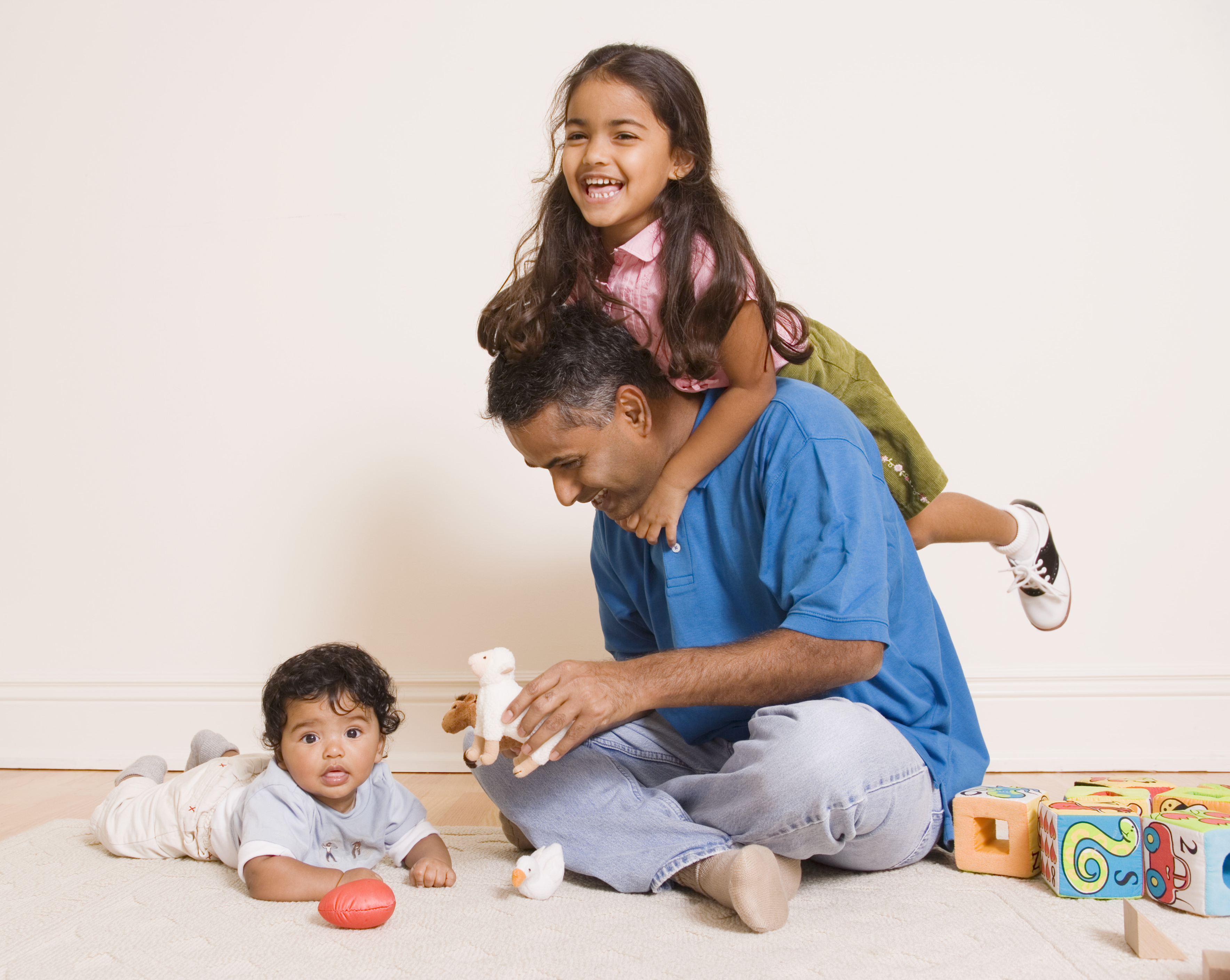 A man sits on the floor, playing with toys with an infant and young girl