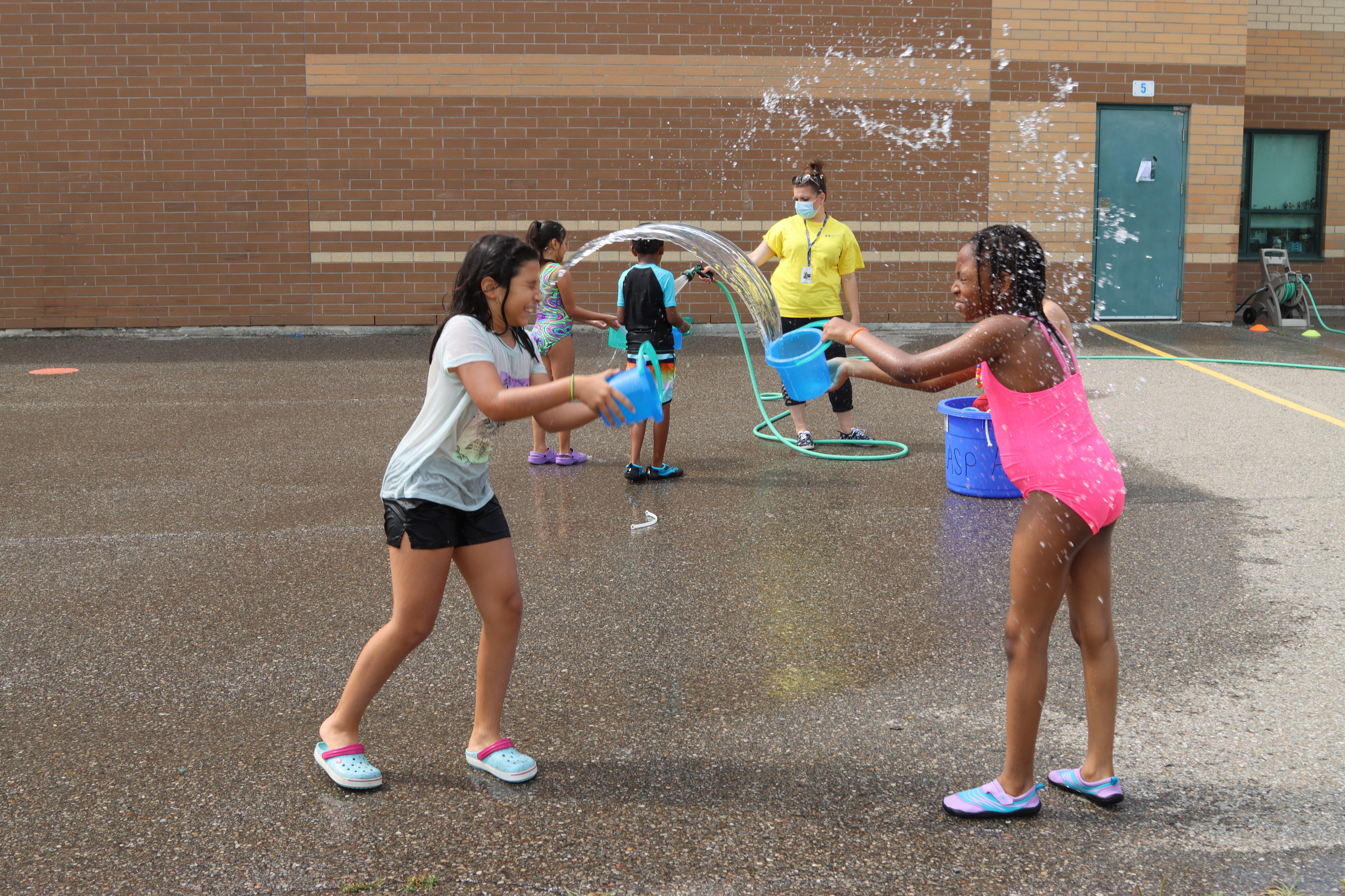 Two girls with buckets enjoy waterplay in a PLASP summer program
