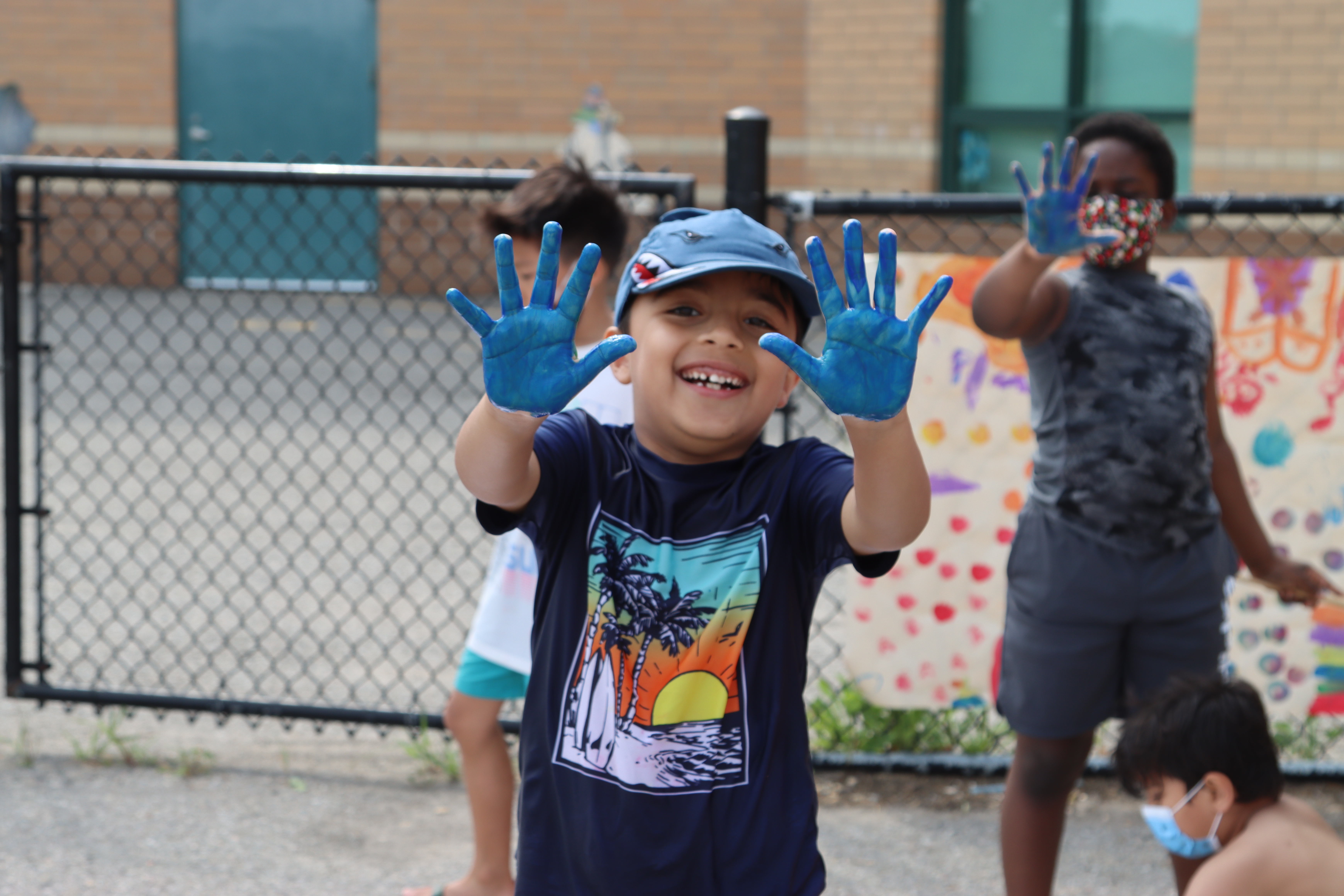 A child holds up his blue palms for the camera and smiles during a PLASP outdoor activity