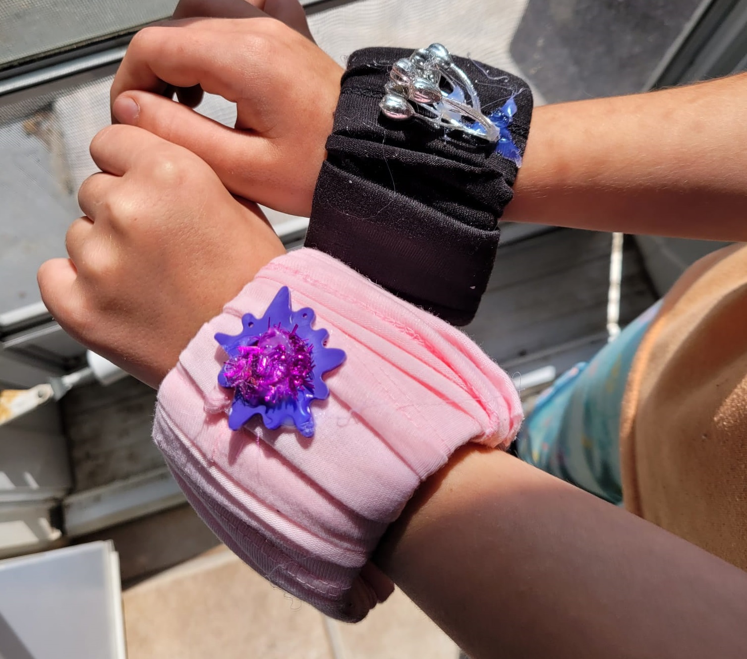 A picture of two bracelets - one wrapped in pink material and one wrapped in black material - both have a sparkly decoration on the top