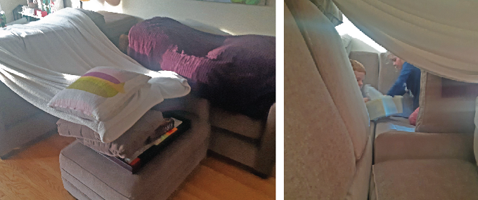 Two young children build a blanket fort on a couch, using pillows and blankets