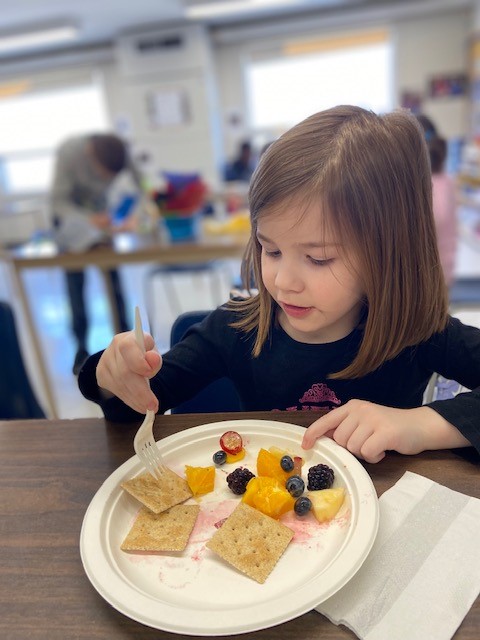 A girl in a PLASP program enjoys a snack of fresh fruit and crackers