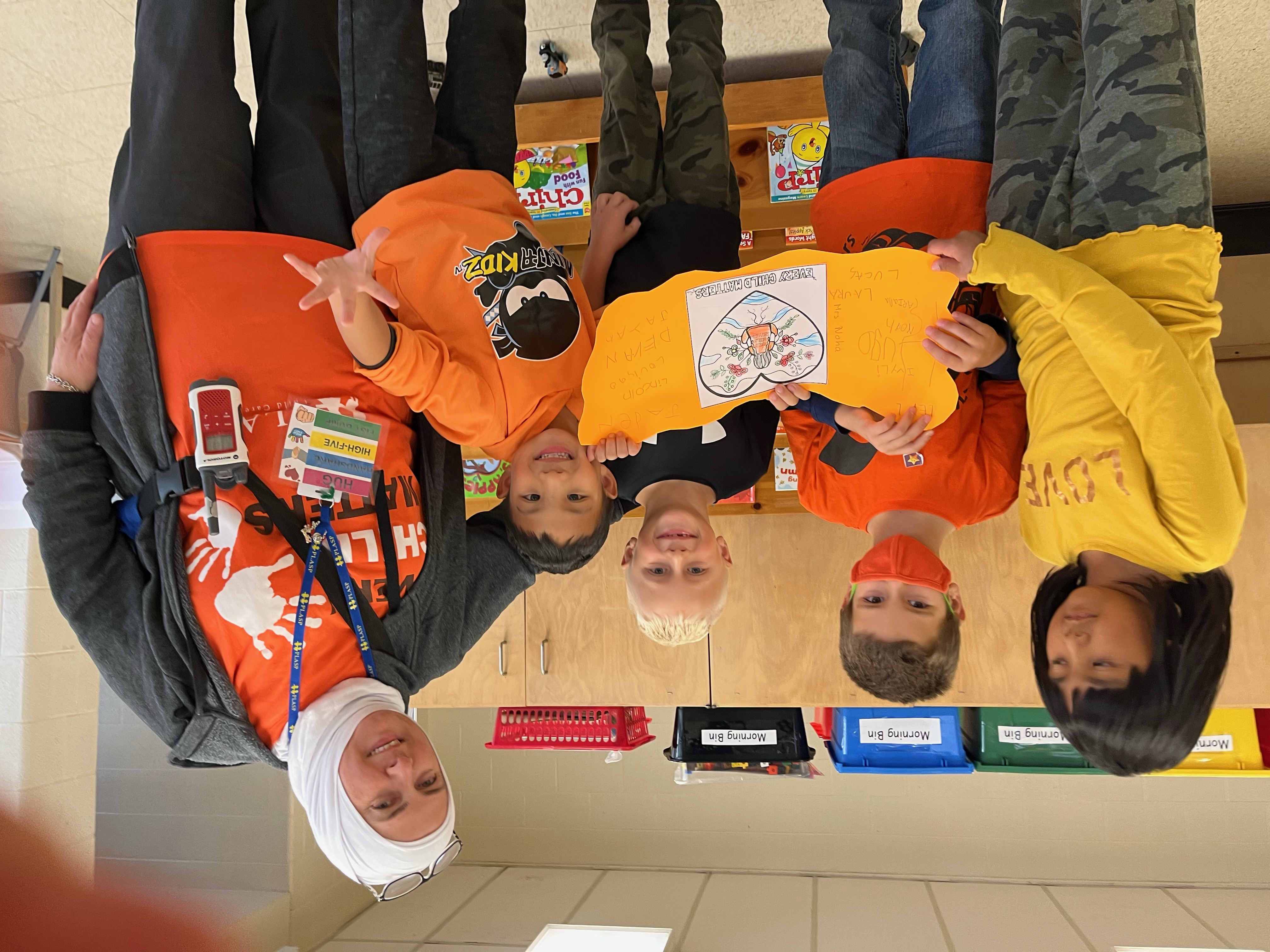 A PLASP educator stands with children in a program, holding up their artwork