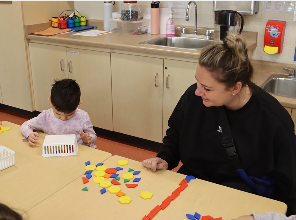 A PLASP educator sits with a young child, who is learning about shapes